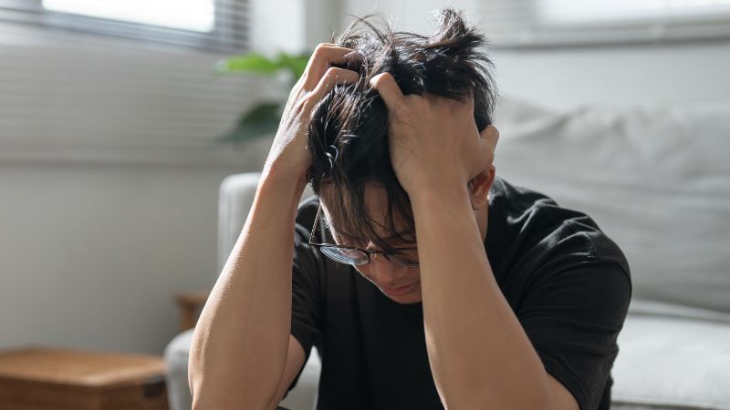 A decorative image of an adult male with his head in his hands, tousling his hair, looking extremely stressed out