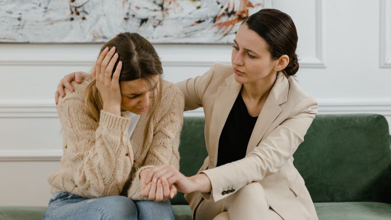 Decorative image of a woman holding her head in her hands while her therapist holds her hand and has another hand over her shoulder