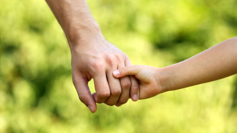 Decorative image of a parent holding their child's hand and walking beside them at a park