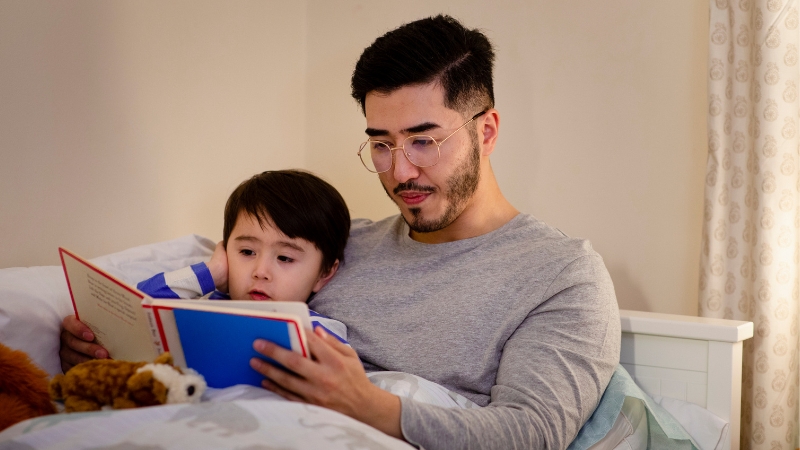 Decorative image of a father in bed, reading a storybook to his child