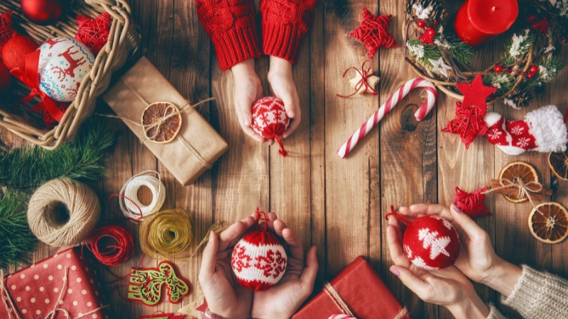 Decorative image of a family stretching their hands and cradling baubles in their hands with candy canes and gifts in the background