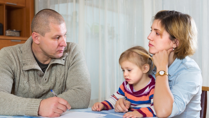 Decorative image of parents deep in thought, seemingly at conflict with each other. Their child sits in her mother's arms.